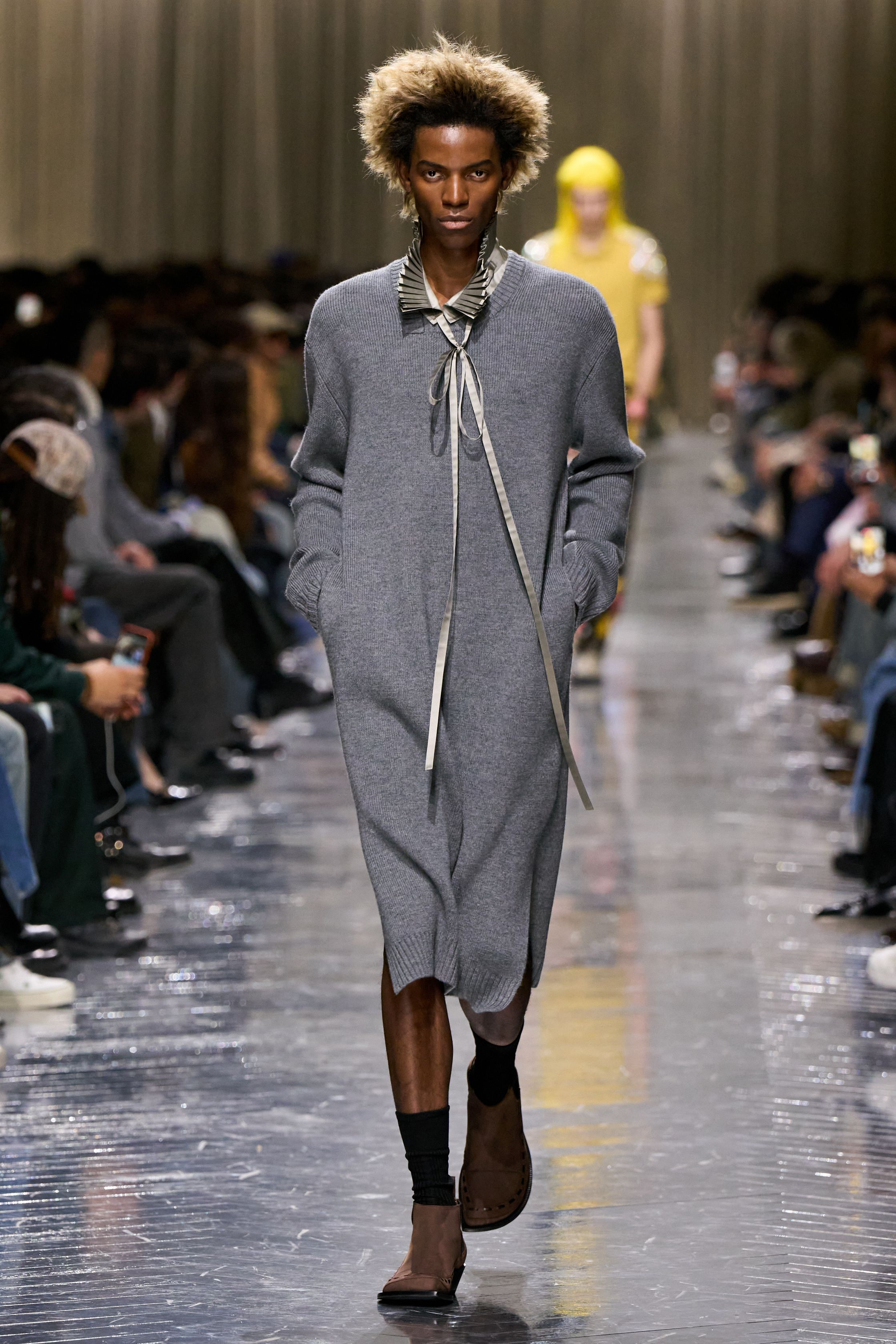 本季 Dior Men 2026 秋冬在克制与叛逆之间建立起新的男性气质坐标。轮廓上，柔软针织、披风式外套与军装结构形成张力对照，模糊正装与休闲、性别与功能的边界；材质层面，羊毛、皮革、毛绒与轻量技术面料并置，强化“触感叙事”。色彩从学院派的灰蓝、橄榄绿过渡至点状印花与手工肌理，传递一种被精心编排的随性。整体呈现出一种“新贵游牧者”形象：既有高级定制的工艺根基，又拥抱当代青年对自由、混搭与身份流动性的渴望-顽石频道趋势研究